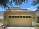 Front view of a two-story home highlighting the attached two car garage and featuring tan paint and lush tree cover at 9126 Lantern Oak Way, Land O Lakes, FL 34638