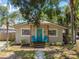 Charming home exterior with a teal front door, covered porch, landscaping and two Adirondack chairs at 1420 W Rambla St, Tampa, FL 33612