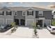A row of gray townhomes with driveways and minimalistic landscaping featuring palm trees, small bushes, and white gravel at 33062 Frosted Clover Way, Wesley Chapel, FL 33545