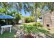 Green backyard with a privacy fence, tropical foliage, and dining table with a blue striped umbrella at 3626 S Hesperides St, Tampa, FL 33629