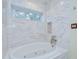 Close up of a bright white bathtub with white marble surround, a window, and brushed metal fixtures at 1931 Jaudon Rd, Dover, FL 33527