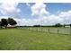 Backyard view of a grassy field with a wooden fence and wooded trees under a blue sky at 14409 Curley Rd, Dade City, FL 33525