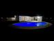 Backyard view of a pool with bright blue lighting, surrounded by concrete, near the white house at 10006 N Connechusett Rd, Tampa, FL 33617