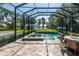 Screened-in pool area featuring a hot tub and lounge area with a tranquil view of the lush green landscape at 16603 Hutchison Rd, Odessa, FL 33556