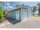 View of the storage shed with two roll up doors, white pedestrian door and gravel area at 16603 Hutchison Rd, Odessa, FL 33556