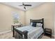 Cozy bedroom featuring a ceiling fan, a window for natural light, and a dark-toned bed with neutral bedding and a small end table at 6154 Marsh Trail Dr, Odessa, FL 33556