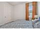 Cozy bedroom with blue-patterned bedding, a window with orange curtains, and neutral colored walls at 8192 Ivy Stark Blvd, Wesley Chapel, FL 33545