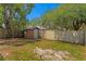 View of fenced backyard featuring a small storage shed, lush green trees, and a partially grassy yard at 13046 Leverington St, Tampa, FL 33624