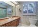 Bright bathroom with floral wallpaper, wood vanity, and natural light from shuttered windows at 1670 Fox Rd, Clearwater, FL 33764