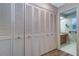 Hallway with multiple louvered closet doors leading to a bathroom with wood vanity and patterned wallpaper at 1670 Fox Rd, Clearwater, FL 33764