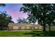 Charming brick home with metal roof, lush lawn, mature trees, and a welcoming front porch under a beautiful pink and blue sky at 17801 Simmons Rd, Lutz, FL 33548