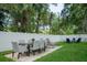 Green backyard featuring an outdoor dining and lounging area, surrounded by a white fence and mature trees at 4710 W Tambay Ave, Tampa, FL 33611