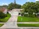 A well manicured home with a large front yard featuring lush green grass, a mature tree, and wide driveway at 1562 Coastal Pl, Dunedin, FL 34698