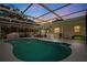 Evening view of backyard pool featuring screened-in lanai, covered patio, and lush landscaping at 1562 Coastal Pl, Dunedin, FL 34698