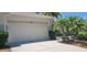 Attached two-car garage featuring a concrete driveway, manicured shrubbery, and tropical palm trees on a sunny day at 834 Tremont Greens Ln # 137, Sun City Center, FL 33573