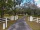 Long paved driveway leading to a gated property with white fencing and mature trees at 12271 Centralia Rd, Weeki Wachee, FL 34614