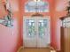 Inviting foyer with decorative glass doors, transom window, tile flooring, and a coral-painted wall at 5100 Lockhart Rd, Brooksville, FL 34602