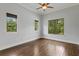 Bright bedroom with hardwood floors, ceiling fan, and three windows offering lush outdoor views at 7713 Still Lakes Dr, Odessa, FL 33556