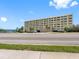 Exterior shot of a multi-story tan building, palms, and partial water view on a sunny day at 100 Bluff View Dr # 404C, Belleair Bluffs, FL 33770