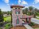 A detailed view of the community entry featuring stone architecture, a tiled roof, and manicured greenery at 4583 Barletta Ct, Wesley Chapel, FL 33543