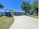Home's exterior features a carport, a long driveway, mature trees, and a neatly maintained lawn at 489 Fox Run Trl, Apollo Beach, FL 33572