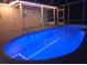 An inviting, glowing, blue in-ground pool is featured at night with a screened lanai and deck at 5435 Birchwood Rd, Spring Hill, FL 34608