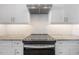A stylish range hood and white backsplash tile highlight a black cooktop atop marble countertops and white cabinetry at 5530 N 9Th St # 6, Tampa, FL 33604