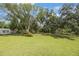 Spacious, grassy backyard with mature trees, a storage shed, and lush landscaping at 5933 Carina Trce, Wesley Chapel, FL 33545