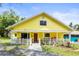 Quaint yellow home featuring a welcoming front porch, vibrant landscaping, and red front door at 2174 62Nd N St, Clearwater, FL 33760