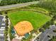 Aerial view of baseball field surrounded by greenery, a nearby road, parked cars, and RVs, highlighting recreational options at 4830 Grand Banks Dr, Wimauma, FL 33598