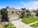 Charming tan two-story home with an attached garage, lush green lawn, and tropical trees at 4852 Trinidad Dr, Land O Lakes, FL 34639