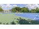 Wide view of blue and green outdoor tennis courts with seating and shade provided by an umbrella at 6334 Spring Flower Dr # 24, New Port Richey, FL 34653