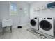 Bright laundry room with two windows, washer, dryer, utility sink, and tile flooring at 718 W Kentucky Ave, Tampa, FL 33603