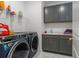 Modern laundry room with gray cabinets, stainless steel washer and dryer, and white marble floors at 13859 Sharp Hawk Dr, Riverview, FL 33569