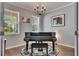 Living room features a black piano, elegant chandelier, and bright windows overlooking the outdoors at 5026 Bromeliad Ave, Wimauma, FL 33598