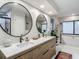 Modern bathroom with double vanity, wood cabinets, round mirrors, and sleek soaking tub under large window at 1014 Sylvia Ln, Tampa, FL 33613