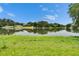 Picturesque view of a calm pond surrounded by verdant grass and mature trees under a blue sky at 16112 N 15Th St, Lutz, FL 33549