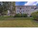Exterior view of the condo with lawn and partial tree coverage with bright blue skies at 2441 Persian Dr # 61, Clearwater, FL 33763