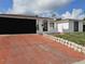 Charming single-story home with a black garage door and a red driveway under a partly cloudy sky at 7834 Treasure Pointe Dr, Port Richey, FL 34668