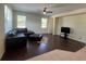 This living room features hardwood floors, two windows, a ceiling fan, and black leather furniture at 11420 Bridge Pine Dr, Riverview, FL 33569