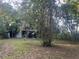 Exterior view of rear of property surrounded by large trees and an overgrown yard at 25425 Olympia Rd, Brooksville, FL 34601