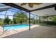 A rectangular pool with clear water surrounded by brick pavers inside a screened enclosure with a view of greenery at 8332 Berkeley Manor Blvd, Spring Hill, FL 34606