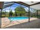 A rectangular pool with clear water surrounded by brick pavers inside a screened enclosure with a view of greenery at 8332 Berkeley Manor Blvd, Spring Hill, FL 34606