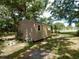 Exterior view of a small, weathered shed with a single door and window nestled among mature trees on a grassy lot at 10308 Fore Dr, Tampa, FL 33612