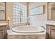 Close-up of a soaking tub with decorative tile surround and a glass block window, creating a spa-like atmosphere at 3656 Kalanchoe Pl, Wesley Chapel, FL 33544