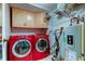 Well-lit laundry room with red washer and dryer, upper cabinets, and modern water heater at 700 Starkey Rd # 1216, Largo, FL 33771