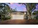 Inviting two-story home featuring a brick driveway, attached garage, manicured landscaping, and mature trees at dusk at 1120 43Rd N Ave, St Petersburg, FL 33703