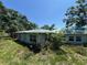 Overgrown exterior featuring a light blue home with a weathered green roof and yellow shuttered windows at 2402 E 148Th Ave, Lutz, FL 33549