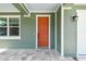 Close up of the vibrant orange front door, complemented by stone tile and green siding at 511 Roanoke St, Dunedin, FL 34698