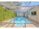 Inviting in-ground pool under a screened enclosure, featuring a unique green wall and brick paver surround at 12222 Meadowbrook Ln, Hudson, FL 34667